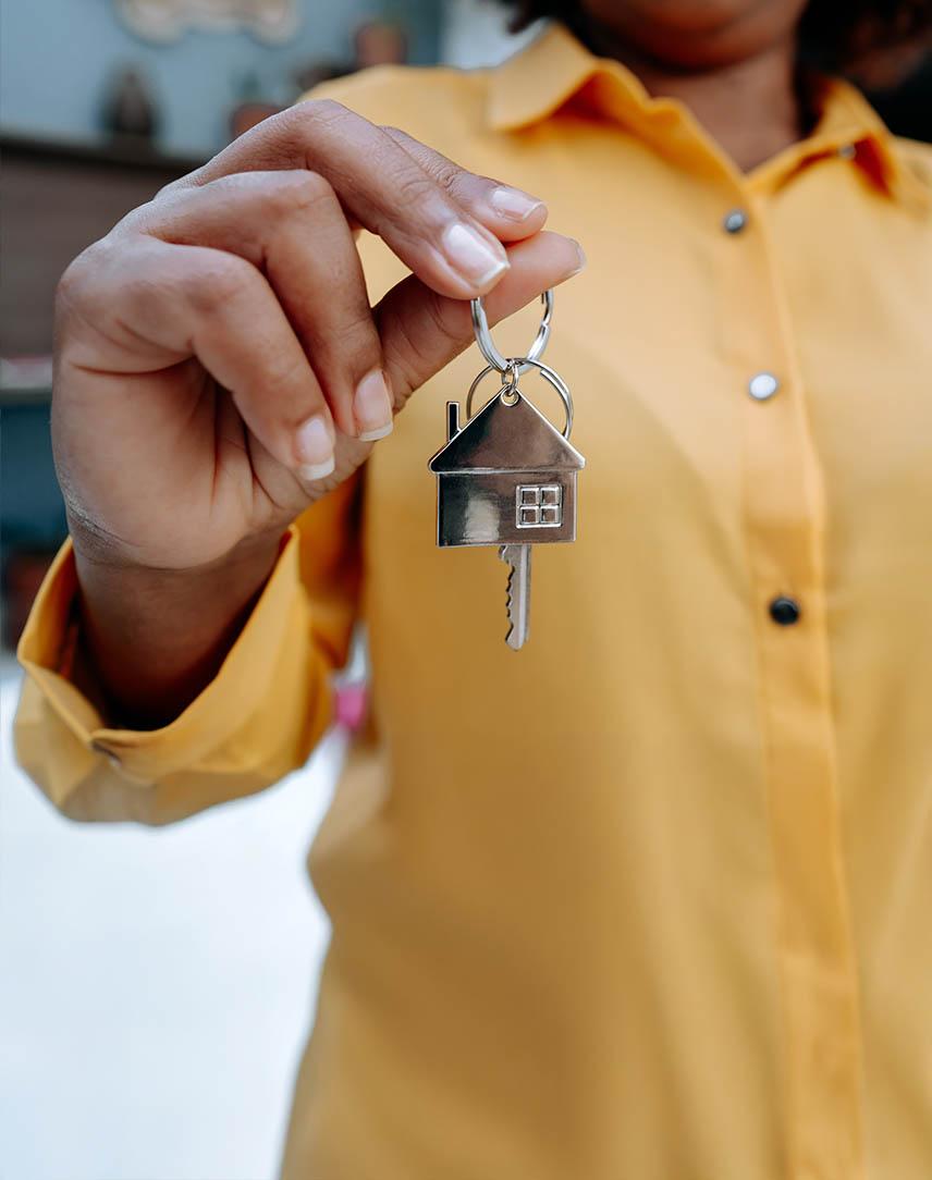 Frau hält einen Schlüssel mit einem Zuhause-Schlüsselanhänger in der Hand